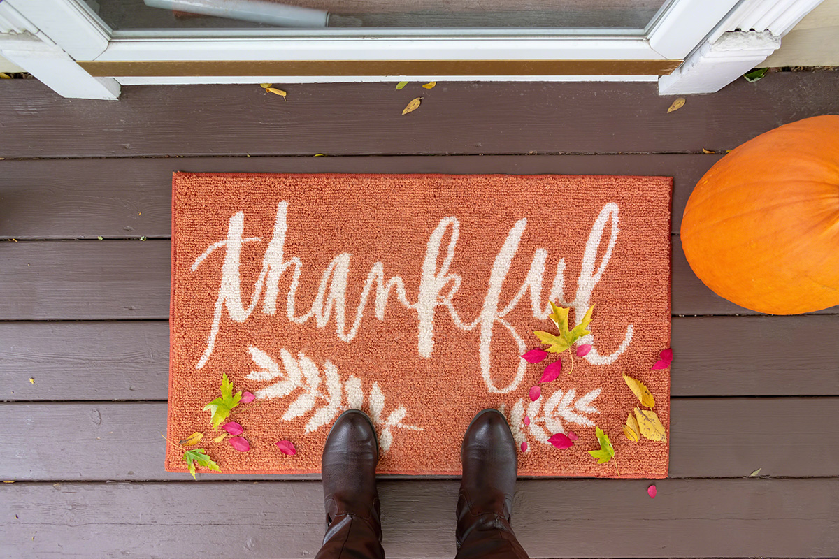A person wearing brown boots stands on a doormat that says "thankful," surrounded by autumn leaves and a pumpkin, in front of a door—capturing the cozy, welcoming spirit often found in Sterling Ranch Colorado.