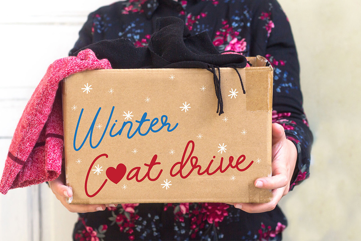 Person holding a cardboard box labeled "Winter Coat Drive," filled with a red and a black item of clothing, helping to support the Sterling Ranch community in the Denver metro area.