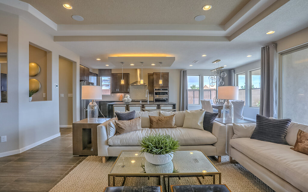 Modern open-concept living room and kitchen in Sterling Ranch CO, featuring beige sofas, a glass coffee table, neutral decor, and large windows letting in natural light—an inviting retreat just southwest of Denver.