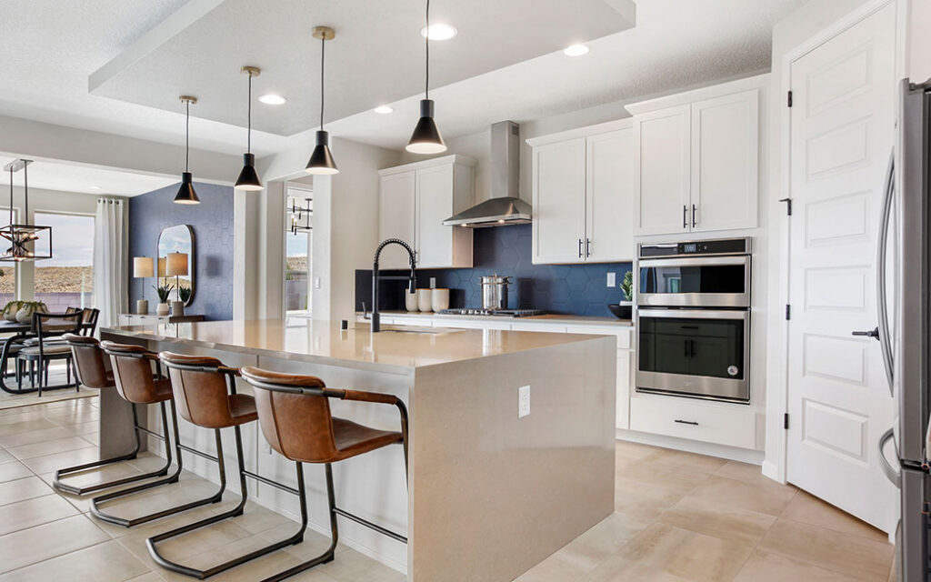 Modern kitchen with a large island, brown leather barstools, pendant lights, white cabinets, stainless steel appliances, and beige tile flooring. The dining area is visible in the background, reflecting the stylish and contemporary ambiance found in many homes throughout Sterling Ranch Colorado.