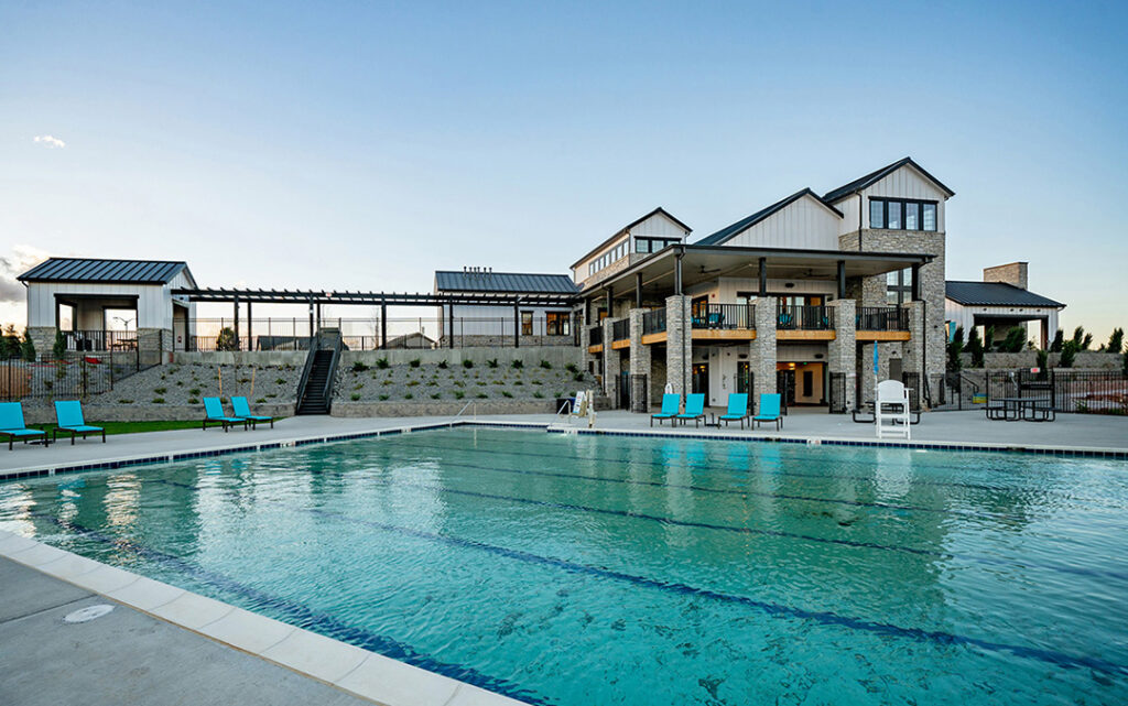Outdoor swimming pool with clear water, surrounded by blue lounge chairs, in front of a modern two-story clubhouse at sunset—perfect for relaxing evenings in the heart of Sterling Ranch CO, part of the vibrant Denver metro area.