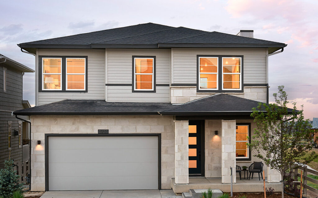 Modern two-story house with a light stone and siding exterior, large windows, a double garage, and a small front porch with two chairs at dusk—perfectly nestled in the desirable Sterling Ranch neighborhood of Littleton, CO.