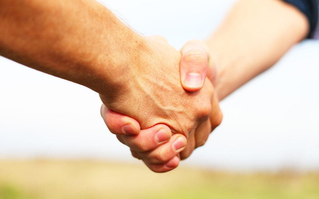 Two people shake hands outdoors in Sterling Ranch Colorado, with a blurred background.